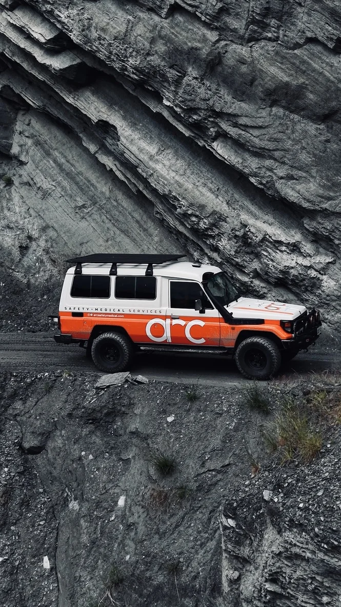 Arc Safety + Medical 4WD vehicle on a narrow road beneath a rocky cliff